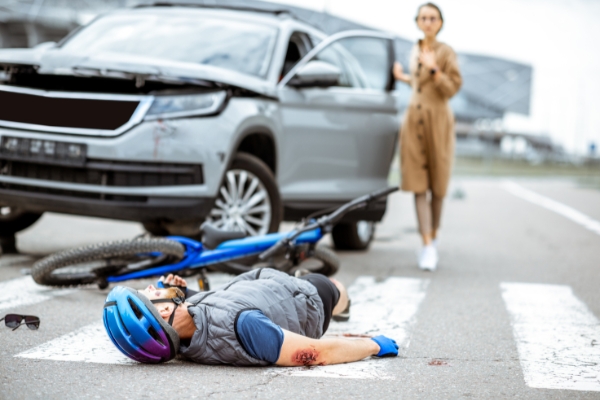 A biker lying down on the street with his bicycle beside him after being hit by the car behind. 