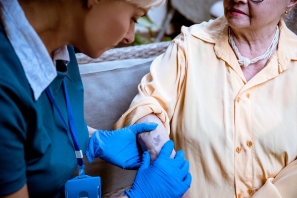 A nurse looking at a bruise in the arm of an old woman.