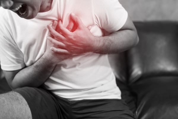 A man clutching his chest and experiencing chest pain as a sign  of post-surgery complications.