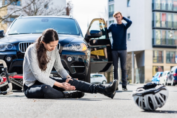 A female pedestrian sitting on the road and clutching her leg in front of a car and it's driver. An accident that can be grounds for pedestrian accident claims.