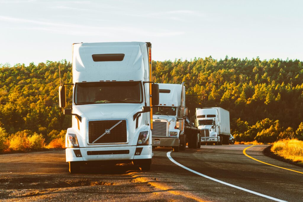 Three white semi trucks sitting on the side of a road